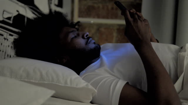 Hombre-africano-usando-smartphone-en-la-cama-por-la-noche