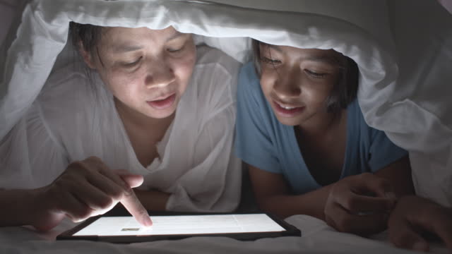 Familia-asiática-con-madre-e-hija-Mirando-la-tableta-en-una-manta-en-la-cama-en-casa