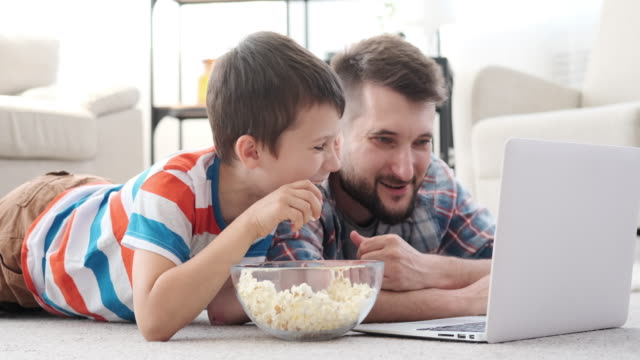Padre-e-hijo-riendo-mientras-mira-la-película-en-el-ordenador-portátil