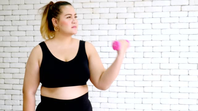 Overweight-young-woman-in-sportswear-exercising-with-dumbball-at-home