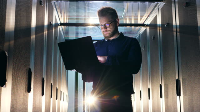 IT-support-engineer-in-glasses-is-operating-a-laptop-in-a-server-room