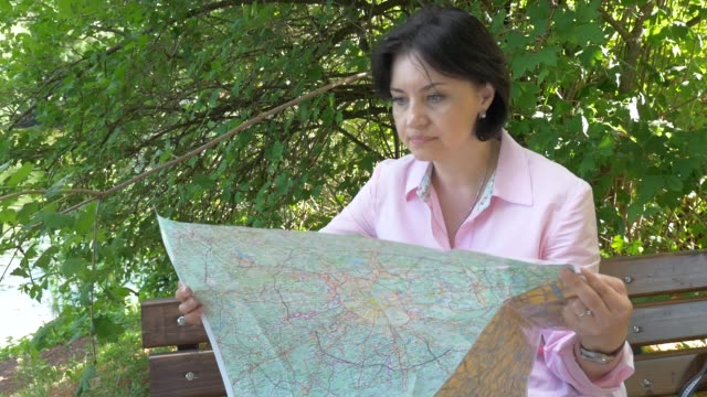 Brunette-looks-at-a-paper-map-in-the-park-near-the-pond
