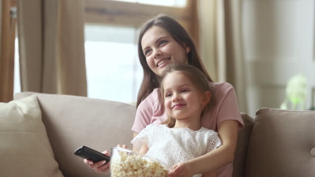 Mother-holding-remote-control-watching-tv-with-small-kid-daughter