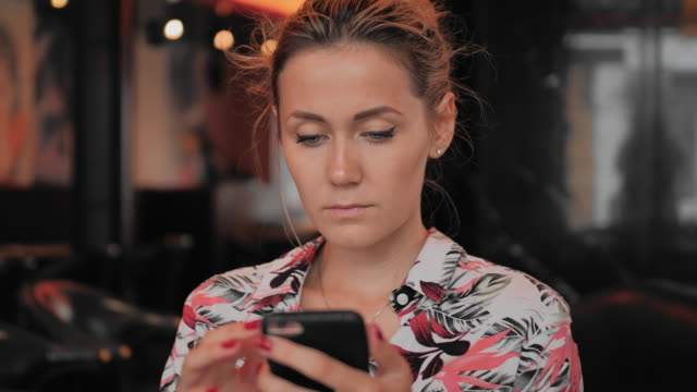 La-joven-mujer-caucásica-utiliza-un-teléfono-inteligente-mientras-se-sienta-en-un-restaurante.-Slow-Motion