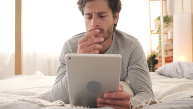 Hombre-confundido-usando-tableta-digital-en-la-cama