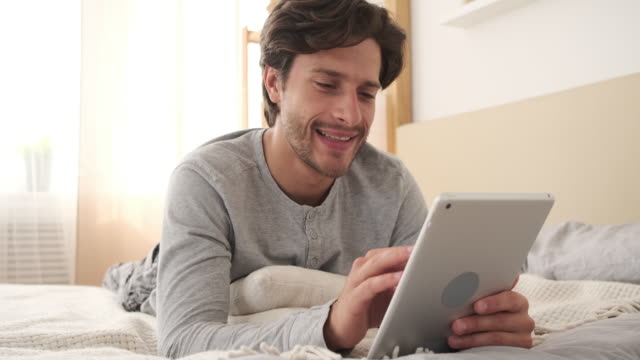 Hombre-alegre-usando-tableta-digital-en-la-cama
