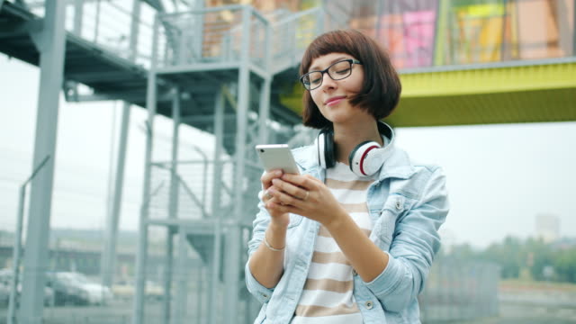 Glückliche-junge-Dame-berührt-Smartphone-Bildschirm-steht-ausdors-in-der-Stadt-allein