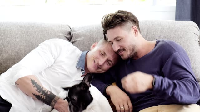Gay-couple-relaxing-on-couch-with-dog.-Enjoy-feeding-a-dog.