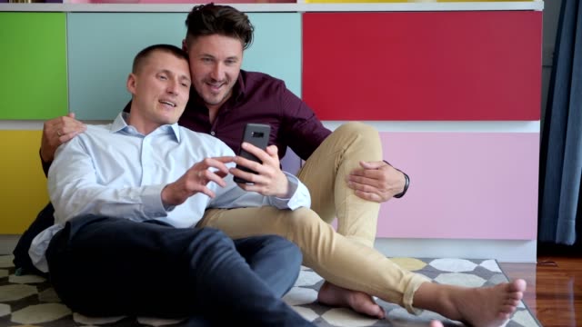 Pareja-gay-usando-teléfono-en-sillón-juntos.-Videollamada-a-amigo.