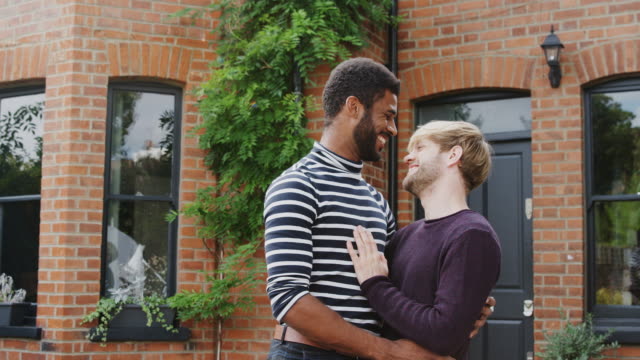 Retrato-de-pareja-gay-masculino-de-pie-fuera-de-un-nuevo-hogar-en-el-día-de-mudanza-juntos-besándose