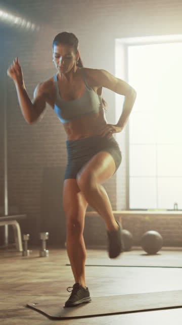 Starke-und-fit-schöne-athletische-Frau-in-Sport-Top-und-Shorts-macht-Standing-March-Übungen-in-einem-Loft-Stil-Industrie-Gym-mit-motivierenden-Postern.-Vertikale-Bildschirmausrichtung-Video-9:16