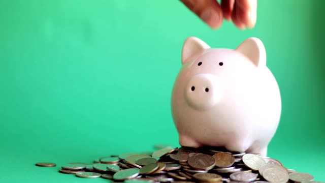 Man-putting-coins-in-piggy-bank-standing-in-pile-of-coins-on-green-background