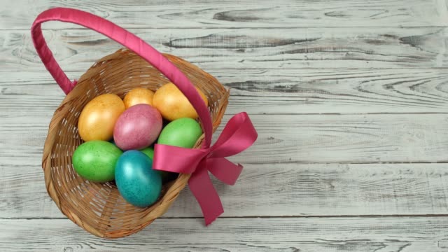 A-man-cleans-a-gift-basket-with-colorful-Easter-eggs-from-a-wooden-table,-copy-space,-decoration