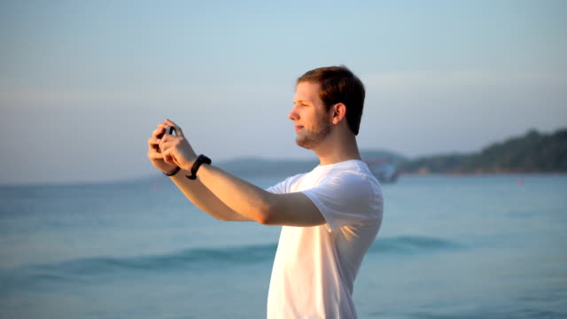Tourist-Taking-Holiday-Photos-of-Tropical-Island-Beach-and-Ocean-During-Colorful-Sunset-With-Smartphone