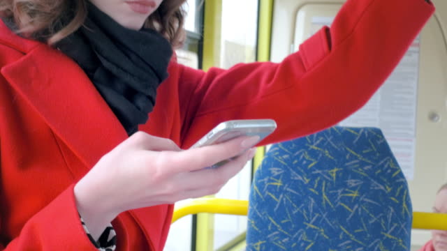 Portrait-of-an-elegant-young-girl-in-a-red-coat.-Uses-a-smartphone-in-public-transport.-Prints-a-text-message-on-the-bus