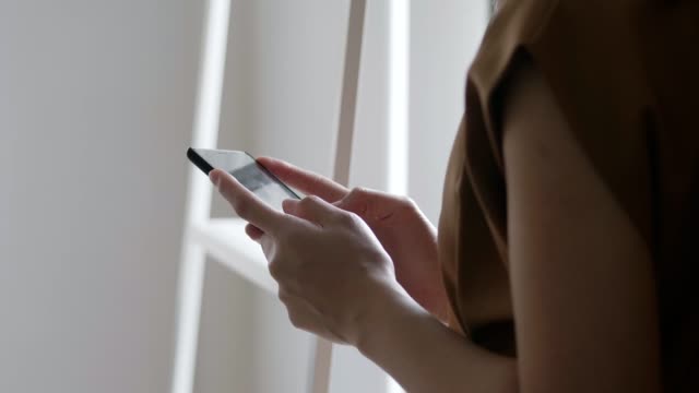 Nahaufnahme-Hände-junge-asiatische-Geschäftsfrau-hält-Tippen-Handy-und-scrollt-durch-Social-Media-Feed-in-Smartphone-neben-Deminhaus-stehend.