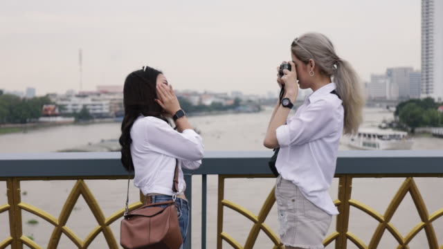 Happy-Asian-lesbian-couple-taking-a-photo-while-standing-on-the-bridge.-Beautiful-Asian-women-traveling-with-a-friend's-vacation-lifestyle.