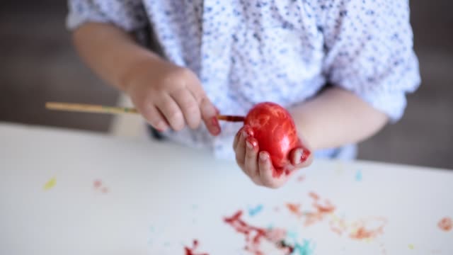 Die-Hände-eines-litlle-Kindes-mit-einem-Pinsel-malen-ein-Osterei-in-roter-Farbe-auf-den-Tisch.