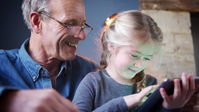Nahaufnahme-von-Enkelin-mit-Großvater-im-Stuhl-spielen-auf-digitalen-Tablet-zu-Hause-zusammen