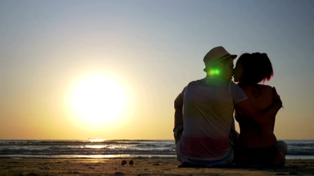 Young-loving-couple-sitting-on-a-beach-and-kissing