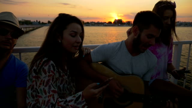 Amigos-cantando-en-verano-con-una-guitarra-en-un-puente-en-cámara-lenta