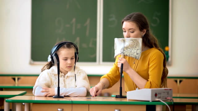 Young-girl-and-teacher-using-headphones-and-microphone-in-the-classroom