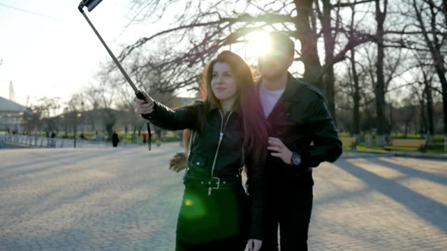 couple-takes-photo-on-mobile-gadget-in-selfie-stick,-phone-on-self-stick,-stylish-guy-girl-walk-in-park