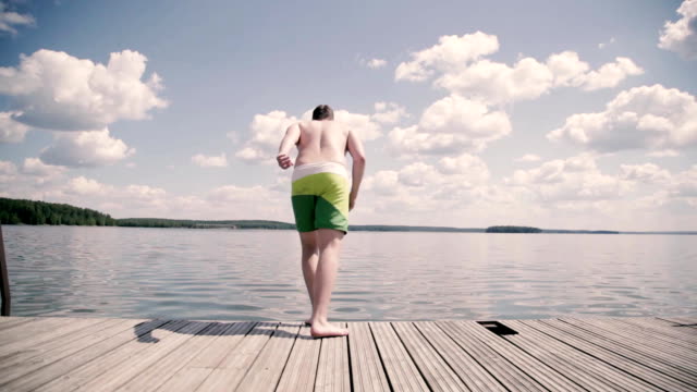 Overweight-guy-dives-on-the-pier-in-a-lake-summer