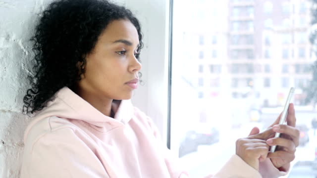 Mujer-afroamericana-Smartphone,-sentado-en-la-ventana-de-navegación
