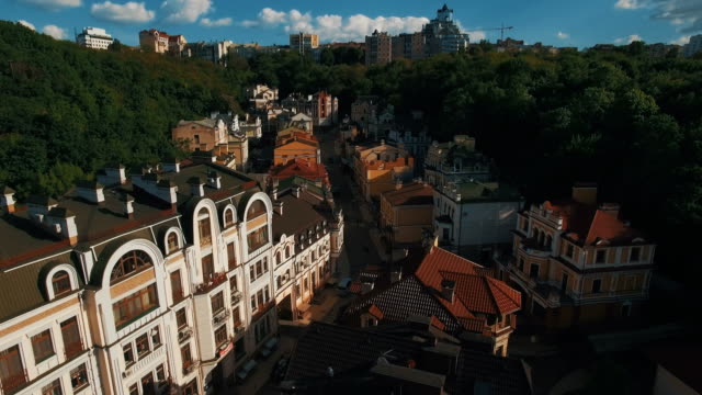 Zángano-de-la-cámara-se-mueve-bajo-techos-de-edificios-en-antigua-europeas-callejuelas-con-casas-de-colores-y-los-peatones-al-atardecer-4K