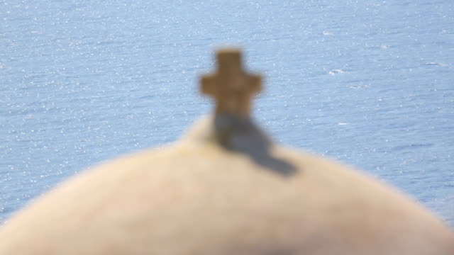 Ruined-fortress-wall,-cross-on-top-of-church-dome-against-blue-sunlit-sea,-sunny