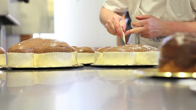 pastry-chef-hands-garnish-Easter-sweet-bread-cakes-with-piping-bag,-closeup-on-the-worktop-in-confectionery