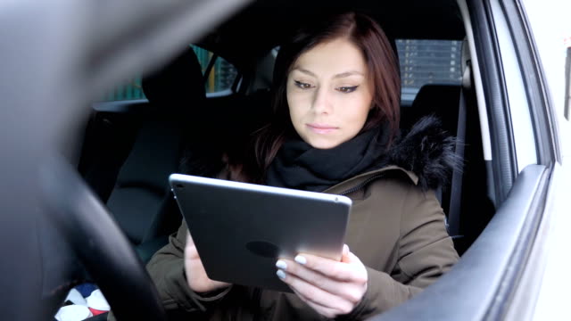 Junge-Frau-eingeben-Nachricht-auf-Tablet-beim-Sitzen-im-Auto