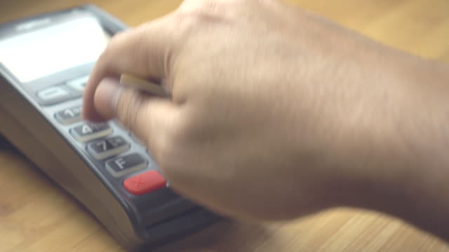 Man's-hand-pushing-the-button-and-swipe-credit-card-payment-on-terminal-standing-on-wooden-desk