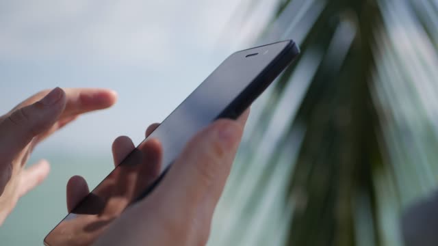 Mujer-manos-smartphone-sobre-árboles-de-mar-y-palmeras-de-fondo.-Chica-tocar-pantalla