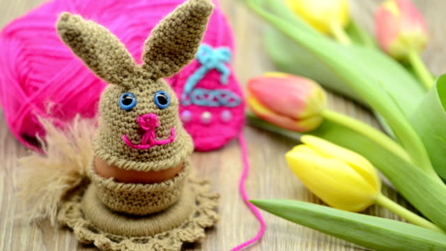 Häkeln-Sie-Ostern-Hase-Eierbecher-aus-Wolle-gefertigt.-frische-Tulpen-und-Wolle-Ball-im-Hintergrund