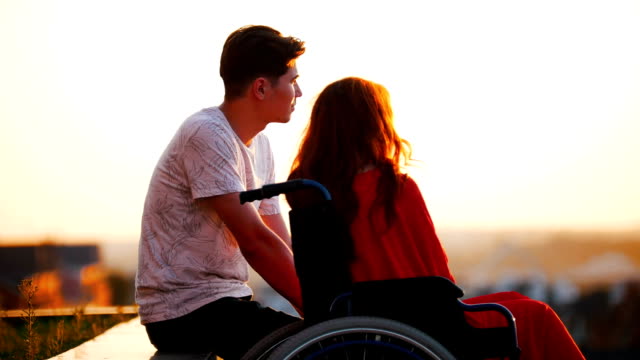 Girl-With-Red-Hair-Is-Sitting-In-A-Wheelchair-And-Boyfriend-is-Sitting-With-Her,-They-Talk-About-Something-And-Look-Into-The-Distance
