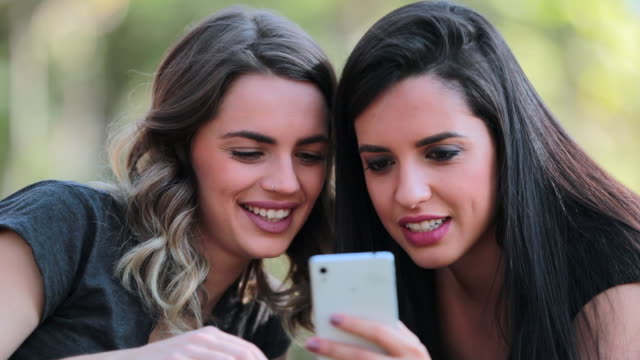 Girlfriends-looking-at-their-cellphones-sharing-social-media-gossip-outdoors