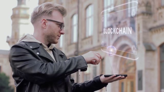 Kluger-junger-Mann-mit-Brille-zeigt-eine-konzeptionelle-Hologramm-Blockchain