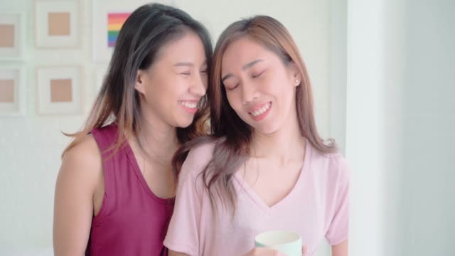 Jóvenes-mujeres-asiáticas-lesbiana-pareja-feliz-hablando-y-tomando-café-en-la-habitación-en-la-casa,-disfrutar-de-momento-de-amor-mientras-está-acostado-en-la-cama-cuando-relajado-en-las-mañanas.-Estilo-de-vida-LGBT-pareja-juntos-en-el-interior-conce