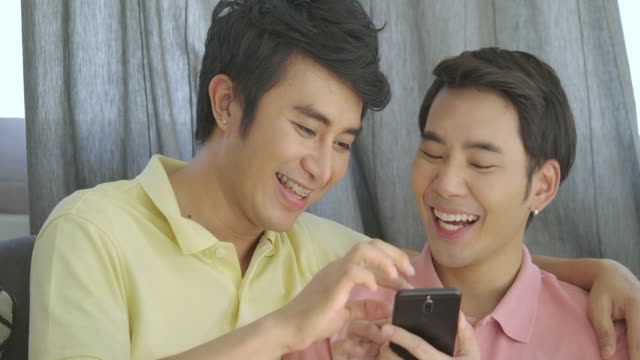 Atractiva-joven-asiática-gay-pareja-relajante-en-casa,-hablando-y-usando-el-smartphone-junto-con-emoción-feliz.