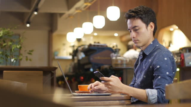 Attraktive-hispanische-junger-Mann-sitzt-allein-in-einem-Café-mit-Laptop-mit-einem-Handy