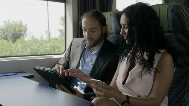 Young-attractive-couple-smiling-and-having-fun-watching-funny-content-on-digital-tablet-while-they-traveling-by-train