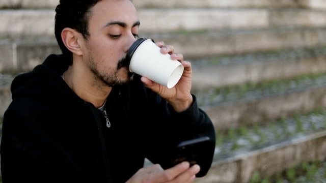 Joven-árabe-hombre-mensajes-de-texto-en-el-teléfono,-bebiendo-café-para-llevar