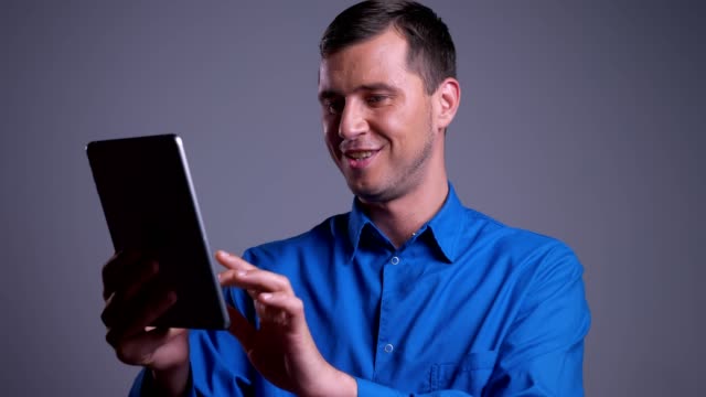 Closeup-portrait-of-adult-happy-caucasian-man-tapping-on-the-tablet-and-smiling-in-front-of-the-camera