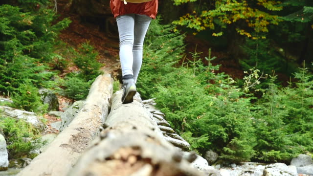 Slender-girl-walking-along-a-log-through-a-mountain-river-in-the-forest