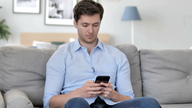 Junger-Mann-nutzt-Smartphone-beim-Entspannen-auf-Sofa