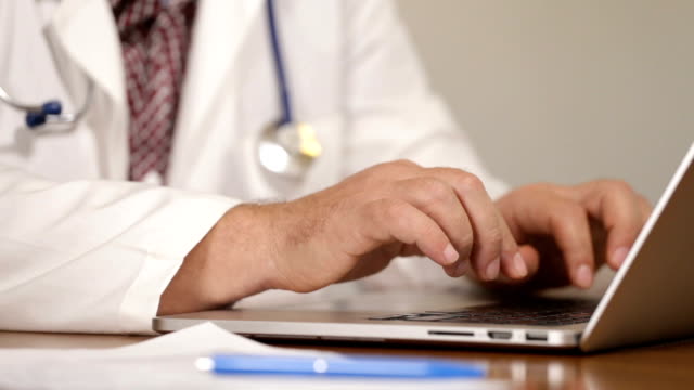 Physician-introducing-patient-medical-data-on-laptop-and-talking-on-mobile-phone,-close-up