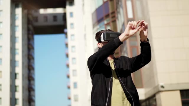 Panning-slow-motion-shot-of-young-man-in-vr-glasses-standing-outdoors-in-city-street-and-working-with-data-and-information-visualized-in-virtual-reality