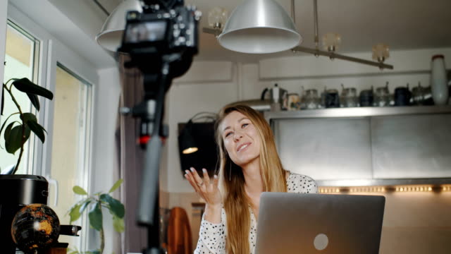 Feliz-profesional-joven-blogger-de-moda-caucásica-filmando-nuevo-video-vlog-con-cámara-en-casa-cocina-cámara-lenta.